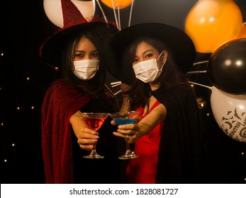 Selective Focus, Two Asian Women In Halloween Costume Wearing Medical Mask Holding Colorful Cocktail Drinks During Pandemic Outbreak Of Coronavirus, Covid-19. New Normal Lifestyle, Halloween Party. 