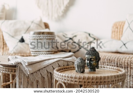 Selective focus at two Buddha statue standing on bamboo coffee table in bright living room interior at bohemian style. Concept mental health and recreation. House with natural materials furniture