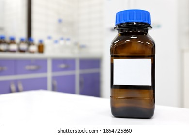 Selective focus of two dark glass reagent bottle with unknown clear liquid chemical inside and blank label in a chemistry laboratory.