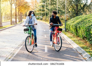 selective focus of two young riding along a bicycle path with a sharing electric bicycle in a beautiful park with many trees at sunset wearing a face mask for the 2020 covid19 coronavirus pandemic - Powered by Shutterstock