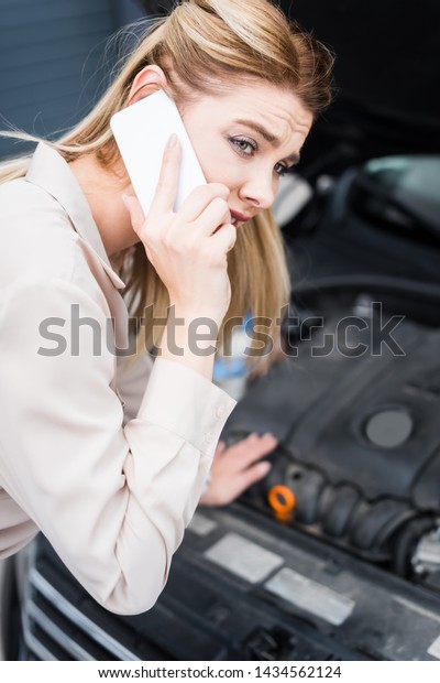 selective focus of\
upset businesswoman talking on smartphone near broken auto with\
open trunk, car insurance\
concept