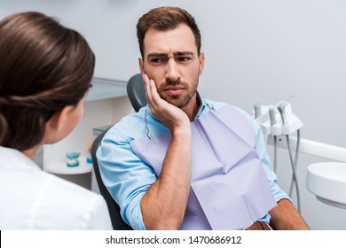 selective focus of upset patient touching face while having toothache near dentist