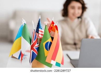 selective focus of various international flags near blurred laptop and language teacher having online lesson at home