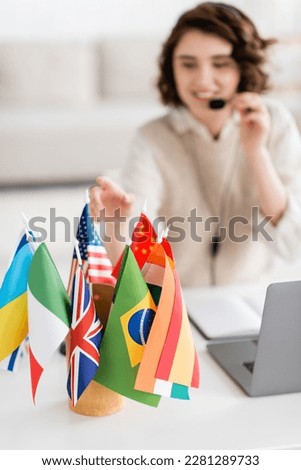 selective focus of various international flags near laptop and blurred language teacher working at home