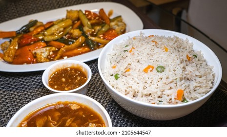 Selective focus of Vegetable Fried Rice in a white ceramic bowl on a meal serving tray with Indo-Chinese foods.
