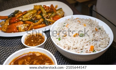 Selective focus of Vegetable Fried Rice in a white ceramic bowl on a meal serving tray with Indo-Chinese foods.