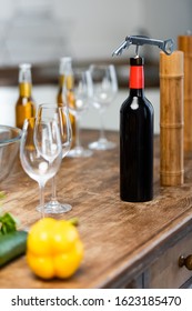 selective focus of vegetables, corkscrew, bottles with wine and beer, wine glasses, Pepper Mill, salt mill on wooden table in kitchen