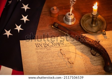 Selective focus view of the constitution of the United States with 13 star flag pistol candle and quill