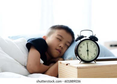 Selective focus at vintage alarm clock show at six o clock and out focus young asian boy sleeping on the bed.