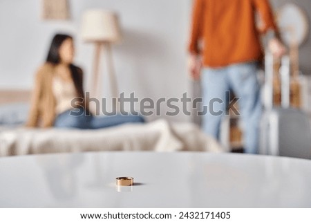 selective focus of wedding ring on table near interracial couple quarreling in bedroom, divorce