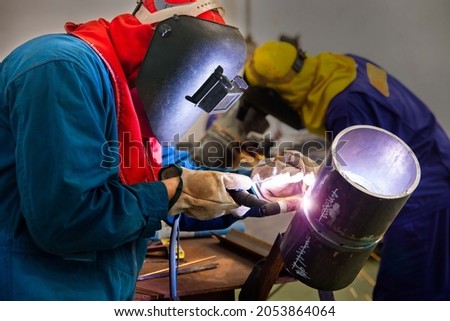 Selective focus to welding area.  Two welder are assembling the workpiece by Tungsten Inert Gas Welding process (TIG). The workers are testing a welding in the workshop.