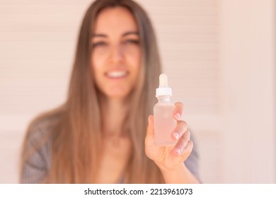 Selective Focus Of White And Clear Hair Serum Bottle In Hand With Blurred Young Woman In The Background