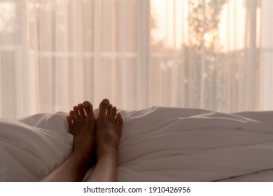 Selective Focus Of Woman Feet On White Blanket In Bedroom In The Morning With Warm Sun Light From Window