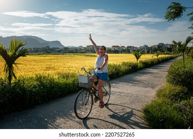 Selective focus. Woman tourist riding a bicycle through rice fields in Vietnam. Young woman riding a bike. Tourist on bicycle in Ninh Binh, Vietnam. Happy woman on her bike - Powered by Shutterstock