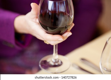 Selective Focus Of Woman's Hand Holding Wine Glass At Restaurant Table