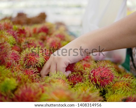 Selective focus of woman's hand picking up rambutans for sale in a supermarket