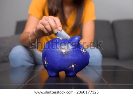 selective focus of woman's hands inserting mexican bills into a piggy bank at home