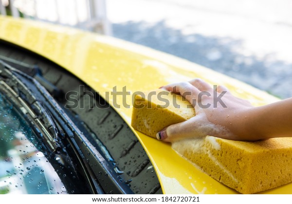 Selective focus at women hand using sponge to wash and\
clean colorful yellow car with soap bubble at home. Self car care\
maintenance activity.\
