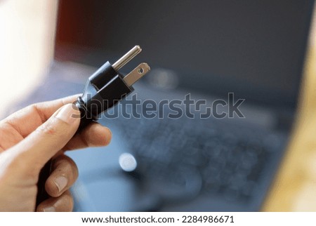 Selective focus. Women's hands are Plug in power outlet adapter cord charger of laptop computer.