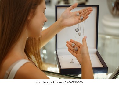 Selective focus of wonderful necklace in hands of female customer in jewelry store. Smiling woman looking at luxurious jewellery and choosing new accessories in shop. Concept of buying. - Powered by Shutterstock