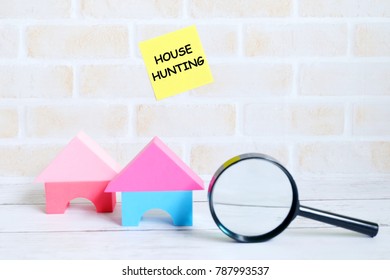 Selective focus of yellow sticky notes written with HOUSE HUNTING with house model and magnifying glass on white wooden background. Real estate theme.