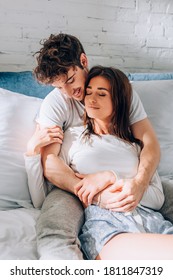 Selective focus of young man hugging girlfriend in pajamas on bed