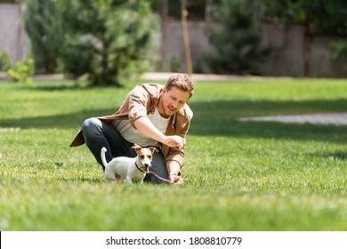 Selective Focus Of Young Man Kneeling Near Jack Russell Terrier On Leash In Park 