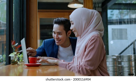 Selective focus, Young muslim woman wearing hijab and young man friend working on laptop, They use laptop computer in coffee shop, muslim business working concept