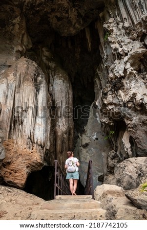 Selective focus. Young tourist entering a huge cave. Tourist touring caves in Thailand. Young woman entering a huge cave in Krabi, Thailand. Stalactite cave in Thailand