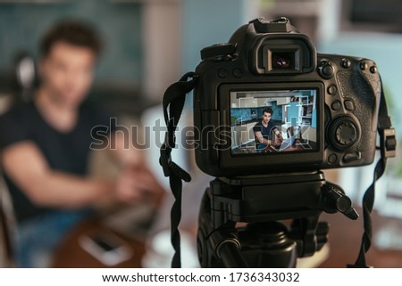 selective focus of young vlogger using laptop while looking at digital camera