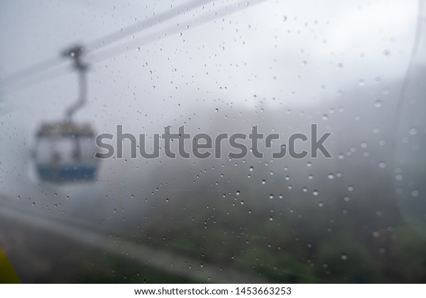 Selective focusing on the\
water drop on the window with blurred mountain and cable car for\
the background.
