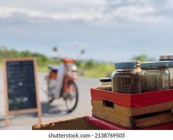 Selective Focus,Wooden Box With Many Coffee Glass Bottle In Against Blurred Outdoor View In Sunshine Day. Outside Park Coffee Shop For Relaxing Time.