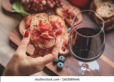 Selective foucs on finger holding ham jamon serrano and glass of red wine  on wooden board