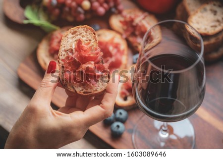 Selective foucs on finger holding ham jamon serrano and glass of red wine  on wooden board