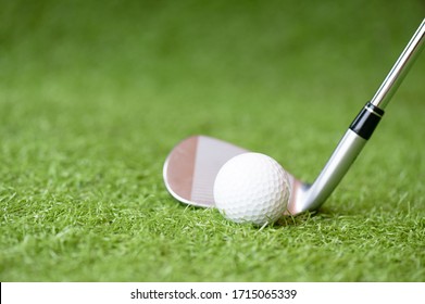 Selective Golf Club And Golf Ball On Green Grass Background.Iron Golf Club Hitting Ball Into A Hole.Outdoor Sport.