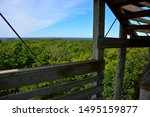 A selective view from the tower at Parnell Tower State Park in Plymouth Wisconsin showing part of the structure along with a beautiful view of trees from a lower observation deck with light clouds. 