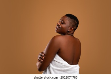 Self Acceptance, Love And Care. Beautiful Smiling Curvy African American Woman With Perfect Skin And Closed Eyes Embracing Herself Isolated On Brown Studio Background, Relaxed Lady Turning Back