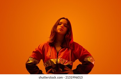 Self Assured Young Model In Trendy Jacket Standing With Hands On Waist And Looking At Camera On Orange Background In Studio