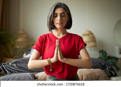 Self awareness and mindfulness concept. Attractive young woman having premature graying meditating at home with eyes closed, focusing on breathing, feeling present moment, making namaste gesture