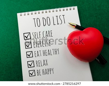 Self Care To Do List Notepad with Red Heart Stress Ball and Pen on Green Background for Health and Wellness Concept. 