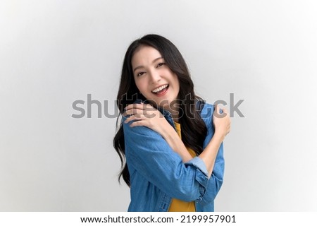 Self care and self esteem concept, Happy young beautiful Asian woman in colorful clothing hugging herself isolated on white background. People emotion portrait concept.