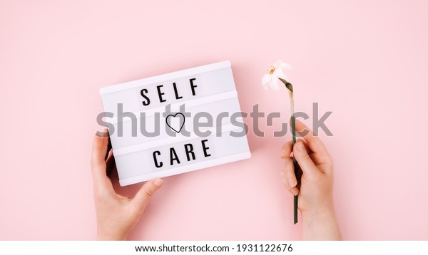 Self Care, Take care of\
yourself, wellbeing routine, self-care activities concept with open\
notebook, flower narcissus and female hand on pink\
background.