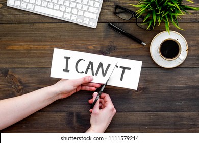 Self confidence concept. Hands cutting the letter t of written word I can't by sciccors. Office desk. Dark wooden background top view copy space