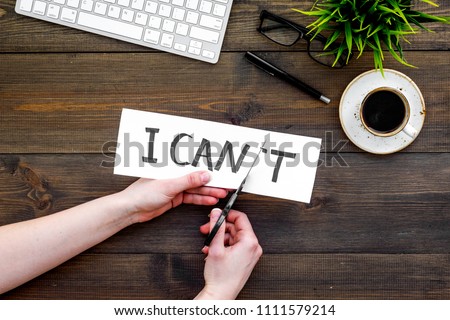 Self confidence concept. Hands cutting the letter t of written word I can't by sciccors. Office desk. Dark wooden background top view copy space