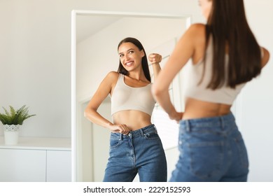 Self confidence concept. Happy caucasian lady pointing finger at her reflection in mirror, having fun while posing after great weight loss, free copy space