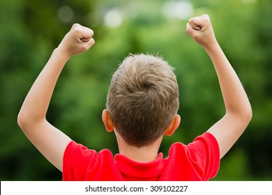 Self confident boy with raised fists celebrating a recent success or victory.