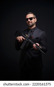 Self Confident Man With Rifle In Black Suit And Sunglasses. Man Holding Assault Rifle. Secret Service Man In Black Suit, Bodyguard Or Special Forces Agent Man With Gun Isolated On Black Background.