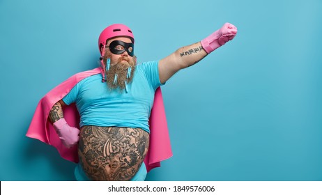 Self Confident Serious Bearded Man Ready To Help People Wears Superhero Costume Pretends Being Heroic Character Has Supernatural Power Stretches Arm Over Blue Background With Empty Blank Space