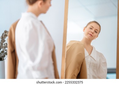 Self confident single woman looking at her reflection in mirror, putting on business clothes. - Shutterstock ID 2255332375