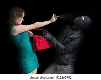 Self defense concept. Young couple is defending with pepper spray against thief in balaclava. Low key photo.